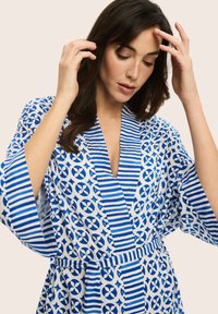 Niebieska i biała szlafrokowa szata z kołnierzykiem w stylu kimona, szerokimi rękawami i zawiązanym w pasie. Posiada okrągłe i paskowane wzory. Gładka tekstura.