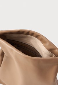 Šviesiai ruda odinė rankinė su minkšta tekstūra, viršuje atsidarantis dizainas ir glotni vidinė dalis. Yra užtrauktukas, skirtas saugiam daiktų laikymui.