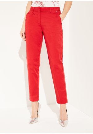 Pantalons en mélange de coton rouge avec une coupe ajustée, dotés de poches latérales et d'un design à jambes droites. Portés avec des chaussures à talons hauts argentées.