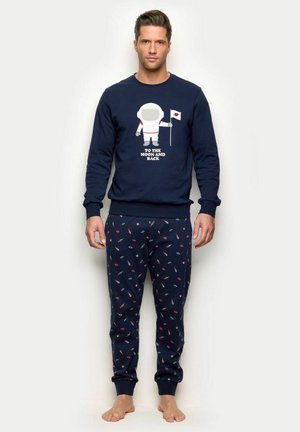 Sudadera azul marino con gráfico de astronauta y texto; combinada con pantalones jogger a juego en azul marino con pequeños patrones coloridos. Corte y tejido estándar.