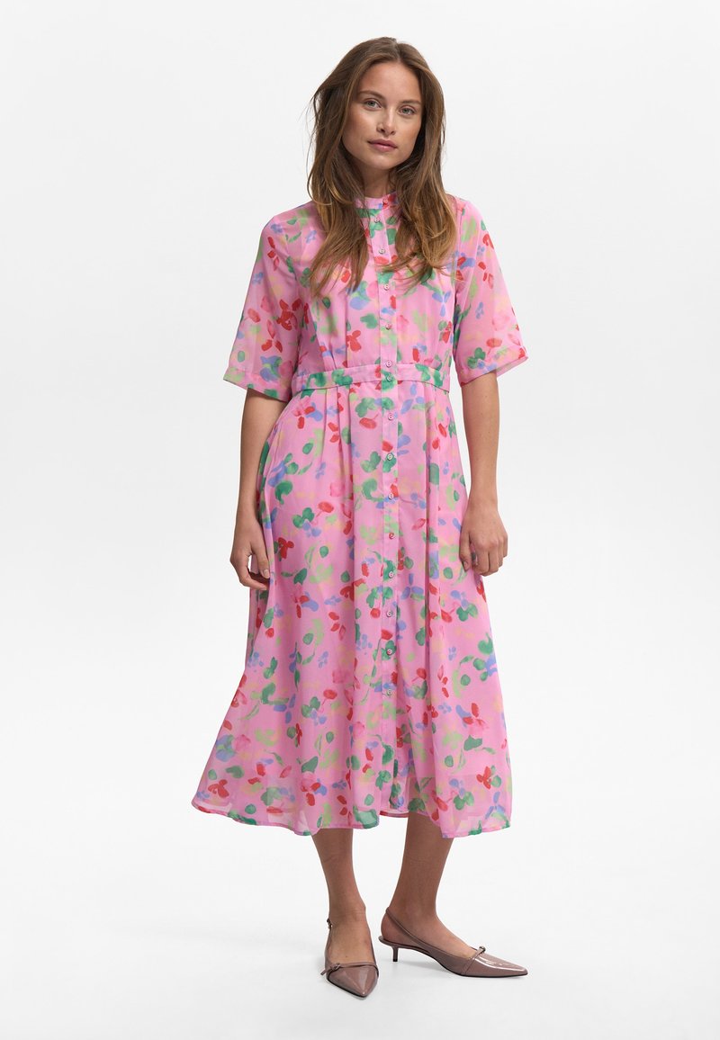 Blommig midiklänning i genomskinligt rosa tyg med korta ärmar, knäppning fram och knyt i midjan. Har röda, gröna och blå blommönster.