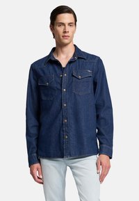 Dunkelblaue Jeanshemd mit langen Ärmeln, spitzem Kragen und zwei Brusttaschen. Mit Messingknopfverschlüssen und gesticktem Saum.