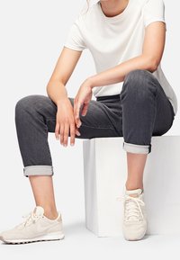 Camiseta blanca de manga corta, jeans grises con vueltas en los puños y zapatillas de color beige claro. Diseño sencillo con textura suave y paleta de colores neutros.