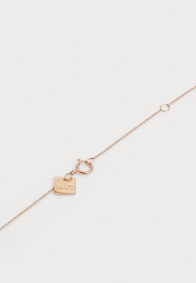 Βραχιόλι σε χρυσό τόνο με λεπτή αλυσίδα, διακοσμημένο με μια τετράγωνη ετικέτα σημειωμένη "18K GINETTE NY" και με κούμπωμα τύπου αστακού.