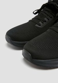 Černé sportovní boty s prodyšným síťovaným svrškem, texturovaným povrchem, plochými šňůrkami a gumovou podrážkou s mírným vzorkem.
