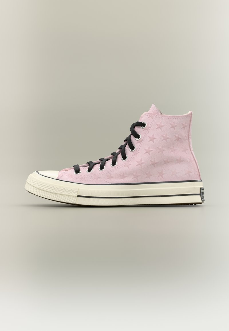 Ροζ αθλητικό παπούτσι με ψηλό πάνω μέρος, ανάγλυφα αστέρια, μαύρα κορδόνια, λευκή καουτσούκ σόλα και μαύρη ρίγα σε ουδέτερο φόντο.