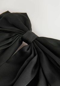 Zwarte satijnen strik met geplooide textuur, voorzien van een brede strik die in een centrale knoop is gestrikt. Gladde oppervlakte en glanzende afwerking.