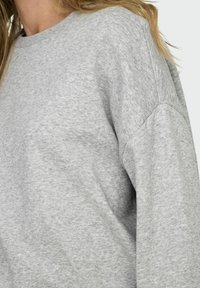 Šedá mikina s kulatým výstřihem vyrobená z měkké texturované látky. Má spadené ramenní švy a volný střih. Klasický design bez vzorů.