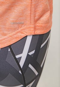 Orange fugttransporterende t-shirt med struktureret finish, parret med højtaljede sorte leggings med et geometrisk hvidt mønster.