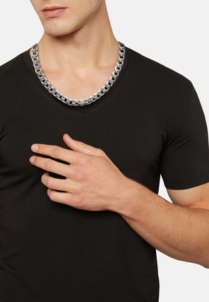 Collar de cadena de plata con eslabones entrelazados, usado sobre una camiseta negra de cuello en V. Textura notable y acabado pulido del collar.