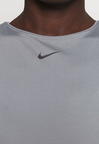 T-shirt de sport gris avec un tissu texturé et un logo Nike noir sur la poitrine. L'encolure est ronde avec un accent rose à l'intérieur.