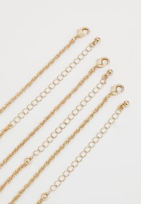 Cuatro collares de cadena de oro con cierres de langosta y eslabones ajustables, dispuestos en paralelo sobre un fondo blanco.