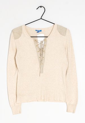 Pull beige à manches longues avec laçage à l'avant et coudières en suède, suspendu sur un cintre noir sur fond blanc.