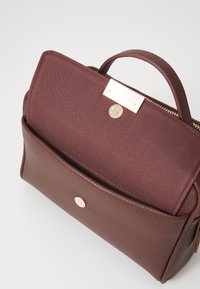 Braune Lederhandtasche mit strukturiertem Finish, weicher Stoffauskleidung, goldenen Hardware-Akzenten und einer Fronttasche mit Verschluss.