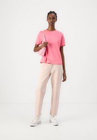 Roze katoenen t-shirt met korte mouwen, gecombineerd met lichtbeige rechte broek. Witte high-top sneakers en een kleine roze schoudertas.