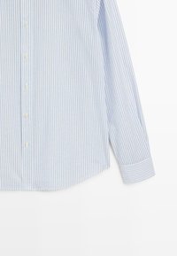 Hellblau-weiß gestreiftes Langarmhemd mit Knopfleiste und Manschetten vor weißem Hintergrund.