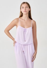 Liliowy dwuczęściowy strój wykonany z lekkiej tkaniny. Posiada cienkie ramiączka, sznurek w talii oraz luźną bluzkę z wiązaniem z przodu.