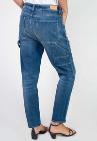 Pantalons cargo en denim bleu avec un design ajusté, poches arrière visibles, une finition texturée et une étiquette sur la taille. Présente une poche latérale supplémentaire.