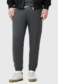 Szare dresowe spodnie z miękkiego materiału o zwężanym kroju, elastycznym pasie i ściągaczach; w połączeniu z białymi trampkami.