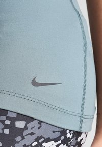 Vaaleansininen urheilu toppi, jossa on kapea koko, sileä rakenne ja litteät saumat. Nike-logo on tummanharmaa vasemmalla puolella.
