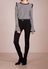 Top manica lunga a righe bianche e nere con dettaglio di ruches sulle spalle, abbinato a jeans skinny neri e stivaletti neri con tacco.