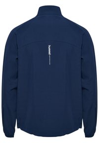 Donkerblauwe lichte jas met een hoge kraag, elastische manchetten en een verticale witte logo op de bovenrug. Glad textuur van de stof.