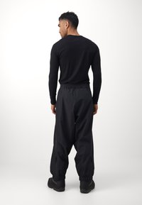 Crna dugoruka majica, opuštenog kroja, uparen s labavim crnim hlačama koje imaju detalje sa patentnim zatvaračem i elastične manžete.