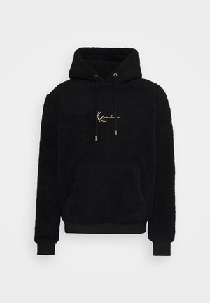 Sweat à capuche en polaire noire avec une texture douce, poche frontale, détails en logo doré et cordons de serrage, présentant un design classique à enfiler.