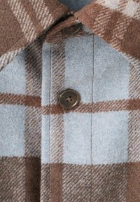 Tela de lana a cuadros marrón y azul con un acabado texturizado, que presenta un cierre con botones y un diseño de cuello puntiagudo.