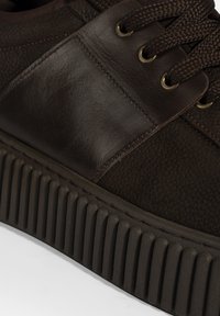 Braune Leder-Sneaker mit strukturierten Einsätzen, runden Schnürsenkeln und einer gerippten Gummisohle. Enthält bronzefarbene Ösen und kontrastierende Nähte.