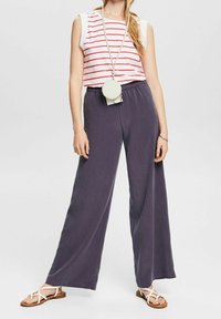 Top sin mangas blanco con rayas rojas, combinado con pantalones anchos de color gris oscuro. La modelo lleva sandalias con tiras y un bolso circular pequeño.