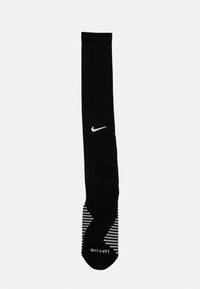 Chaussette Nike noire en matériau extensible, arborant un logo blanc et un motif texturé avec des rayures sur la section du pied. Étiquette "GAUCHE" visible.