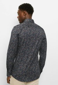 Langärmliges Hemd mit dunkelblauem Grundton und einem bunten Blumenmuster. Der Stoff hat eine glatte Textur, mit einem Standardkragen und enganliegenden Ärmeln.