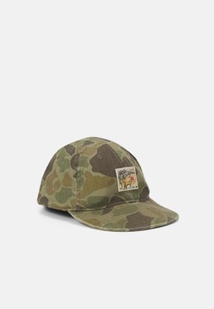Gorra con patrón de camuflaje y un pequeño parche frontal con un perro y el texto «polo expedition 67» sobre un fondo liso.