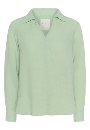 Chemise à manches longues vert clair en tissu texturé avec un col classique et un décolleté en V, offrant une coupe décontractée et des fentes latérales.