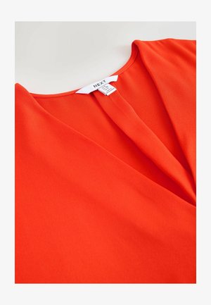 Top roșu cu mâncă și realizat dintr-un material neted, având un decolteu adânc în V și un design fluid. Include un eticheta albă a brandului cu instrucțiuni de îngrijire.