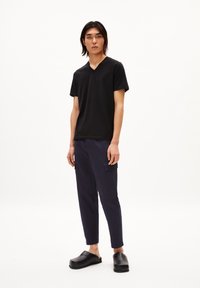 Zwarte v-hals t-shirt, marineblauwe cargobroek met zijzakken en zwarte klompen. Glad materiaal, slim-fit broek, minimalistisch ontwerp.