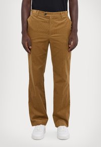 Braune Cordhosen mit geradem Schnitt, ausgestattet mit Taschen vorne, einem einzelnen Knopfverschluss und einer strukturierten Oberfläche. Getragen mit weißen Sneakern.