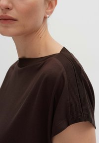 Braunes Baumwoll-T-Shirt mit Rundhalsausschnitt, das über strukturierte Details an der Schulter verfügt. Glattes Material mit kurzen Ärmeln.