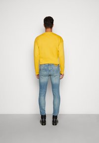 Geel pullover sweatshirt met een ronde hals, gecombineerd met lichtblauwe skinny jeans en zwarte leren laarzen. Gladde stof met een casual pasvorm.
