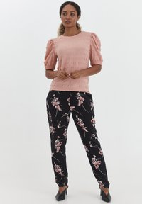 Top rosa chiaro testurizzato con maniche a sbuffo, abbinato a pantaloni neri con stampa floreale che presenta fiori rosa e bianchi, e tacchi neri.