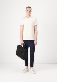 Tricou bej din bumbac, pantaloni navy scurți și încălțăminte albă. Geantă din piele neagră cu un design structurat și mânere duale.