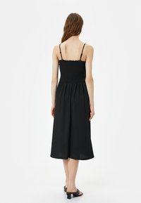 Schwarzes Midi-Kleid mit gerafftem Oberteil und dünnen verstellbaren Trägern. Fließender Stoff und lockere Passform, der unterhalb der Waden endet.