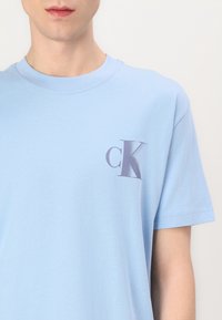 Šviesiai mėlynas medvilninis T-palaidinukas su apvaliu kaklu ir trumpomis rankovėmis. Kairėje krūtinės pusėje yra mažas tamsiai pilkas „cK“ logotipas. Paskirtas maloniam dėvėjimui.