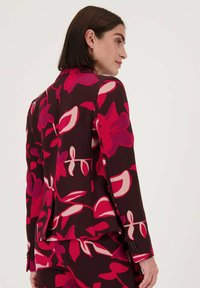 Bloemenpatroon blazer in donker bordeaux met roze en crèmekleurige accenten. Heeft een getailleerde pasvorm, een notched kraag en knoopmanchetten.