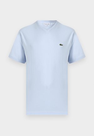 Gaiši zils T-krekls ar V veida izgriezumu un īsām piedurknēm, kreisajā krūtīs neliela zaļa Lacoste krokodila logo.