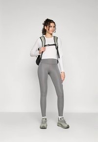 Pilkos tamprės derinamos su baltu ilgarankoviu viršumi ir juodu kuprine. Apranga pasižymi aptakiu dizainu ir lengvomis medžiagomis.