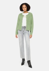 Jasnozielony kardigan z zapięciem na guziki, zestawiony z białym topem z złotym napisem, jasnoszarymi dżinsami oraz czarnymi, spiczastymi botkami.