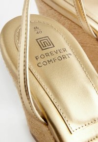 Zlatne wedge sandale s glatkim metalik gornjim dijelom, teksturiranom plutenom unutrašnjošću i urezanom oznakom "FOREVER COMFORT" uz detalje o veličini.