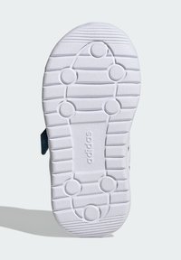 Biela gumená podrážka obuvi s drážkami a kruhovými protišmykovými vzormi. Obsahuje hladký povrch a vyrazené značkové meno "adidas."